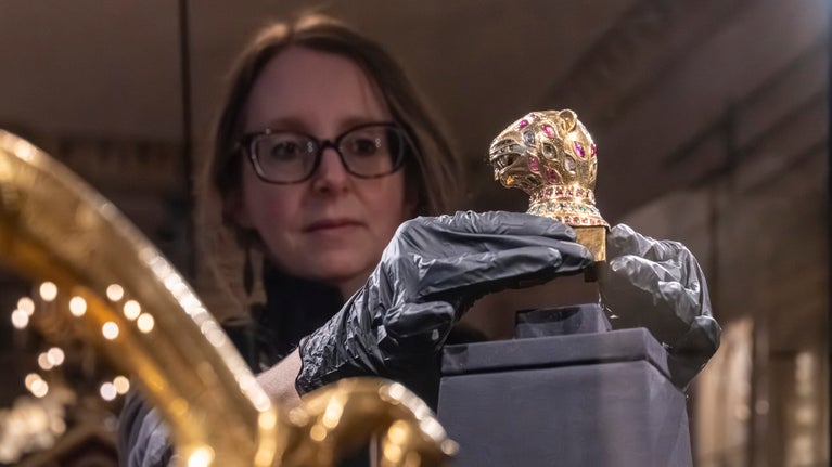 Rheolwr Casgliadau yn gosod y Ffinial Pen Teigr yn ofalus yn cas arddangos newydd